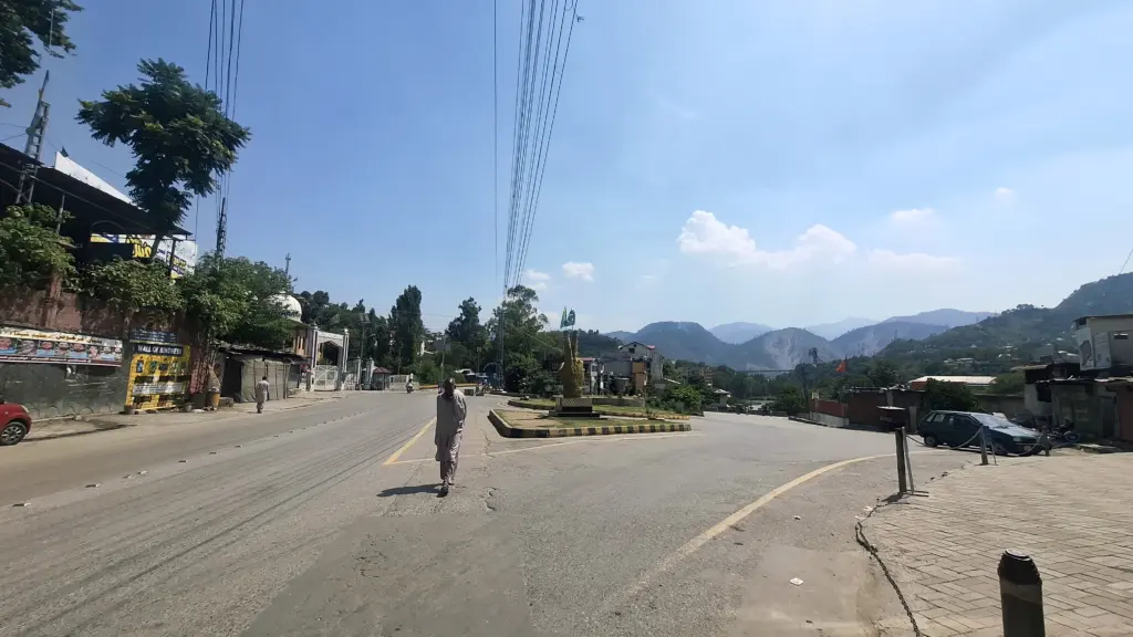 Photo: An elderly resident walks down an empty central roadway in Muzaffarabad during midday heat, amid a region-wide commercial shutdown and traffic suspension.